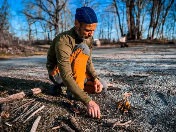 Kleinfeuer brennt auf dem Boden, während ein Mann Zunder hinzufügt