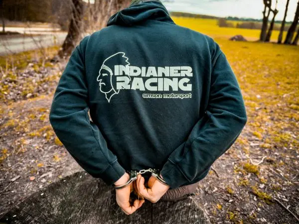 Mann mit Handschellen hinter dem Rücken steht an einem Baumstamm