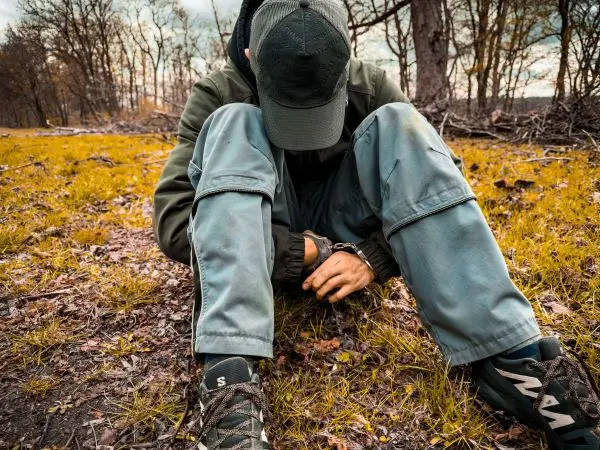 Mann sitzt auf dem Boden und hält seine Hände in Handschellen