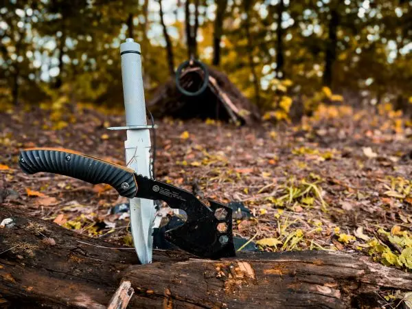 Messer und Axt liegen auf einem Holzstück im Wald