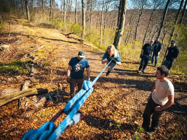Person überquert selbstgebaute Seilbrücke, während andere unterstützen