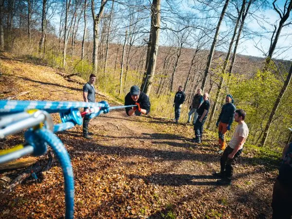 Person zieht an einem Seil, mehrere Personen beobachten im Wald