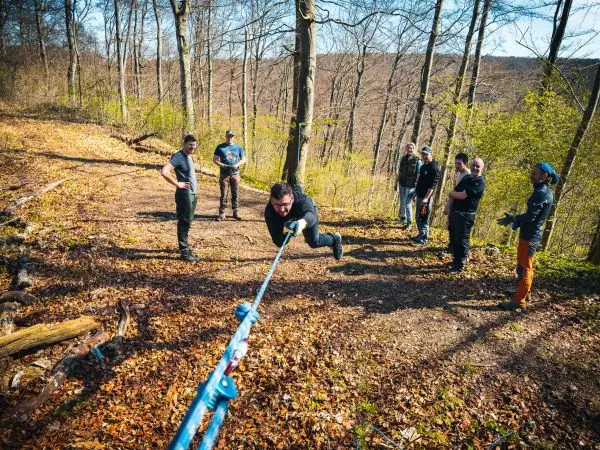 Person zieht an einem Seil, mehrere Personen beobachten im Wald