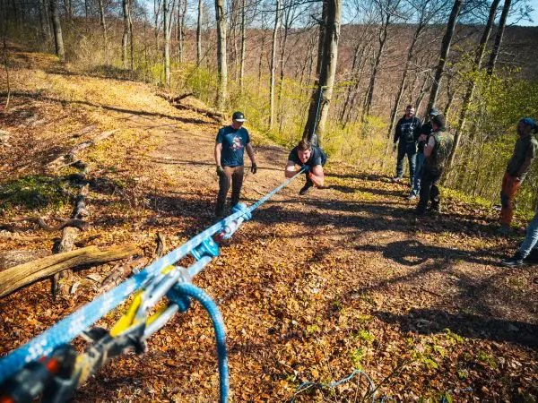 Person zieht an einem Seil, mehrere Personen beobachten im Wald