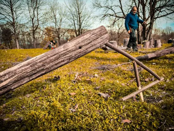 Schlagfalle (Figure-Four) aus Holzstücken im Gras, im Hintergrund eine Person