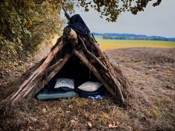 Selbstgebaute Tarp-Notunterkunft aus Ästen mit Schlafmatten im Inneren