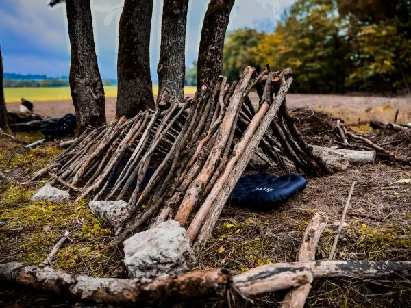 Selbstgebaute Tarp-Notunterkunft aus Ästen und Zweigen zwischen Bäumen