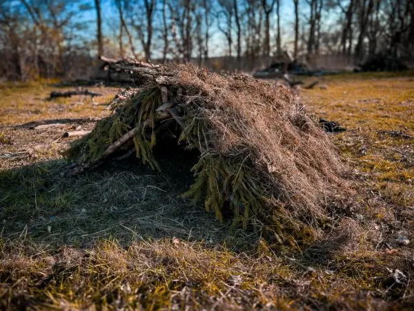 Tarp-Notunterkunft aus Ästen und Gras auf dem Boden