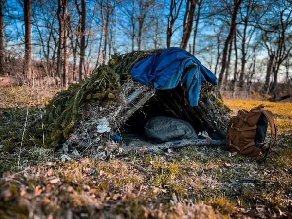 Tarp-Notunterkunft aus Ästen und Moos im Wald mit Schlafsack und Rucksack