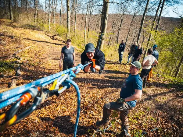 Teilnehmer überqueren eine selbstgebaute Seilbrücke im Wald