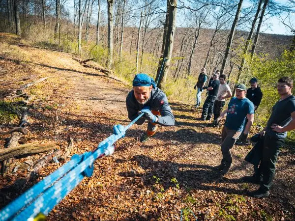 Teilnehmer überquert eine selbstgebaute Seilbrücke im Wald
