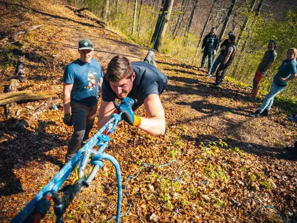 Teilnehmer überquert selbstgebaute Seilbrücke mit Unterstützung von anderen