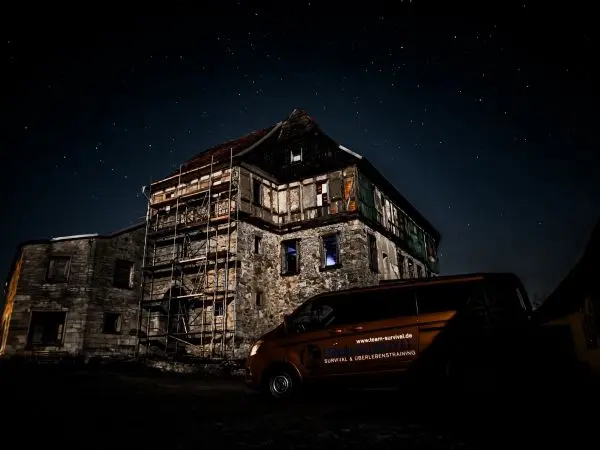 Verfallenes Gebäude mit Gerüst und einem orangefarbenen Fahrzeug im Vordergrund bei Nacht