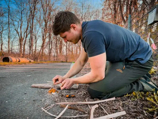 Zunder glimmt auf dem Boden, während ein Mann mit Holzstücken arbeitet
