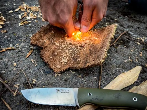 Zunder glimmt auf Holzstück während Hände Funken erzeugen