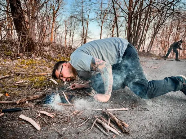 Zunder glimmt zwischen Holzstücken, Rauch steigt auf