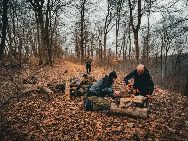 Zunder wird auf einem Holzstück vorbereitet, während andere im Hintergrund stehen