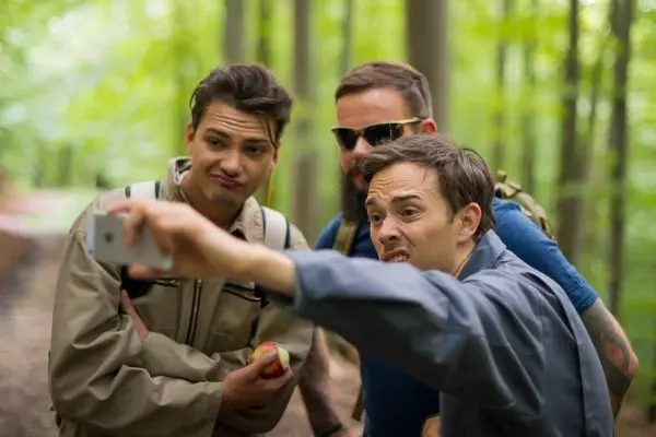 Drei Personen machen ein Selfie im Wald, einer hält einen Apfel in der Hand
