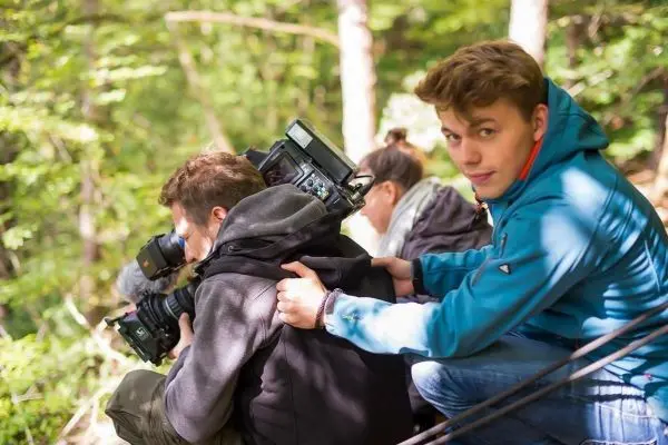 Drei Personen mit Kameras sitzen im Wald auf einem Hang