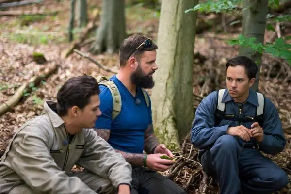 Drei Personen sitzen im Wald auf dem Boden und diskutieren