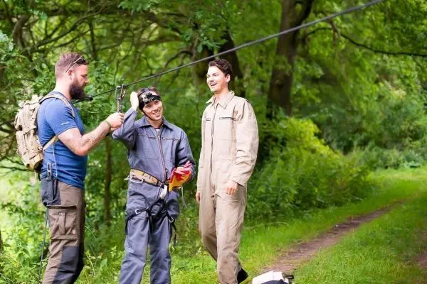 Drei Personen stehen an einem Waldweg und überprüfen eine Seilquerung