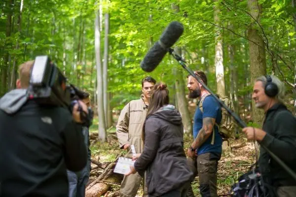 Drei Personen stehen im Wald, während ein Kamerateam Aufnahmen macht