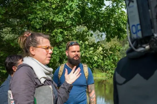 Gruppendiskussion am Ufer eines Gewässers mit Bäumen im Hintergrund