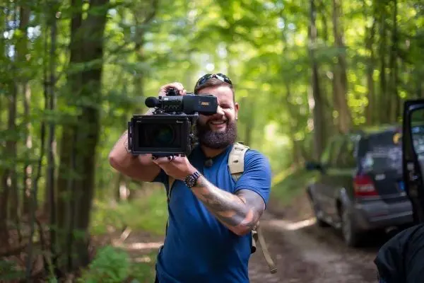 Kameramann hält professionelle Videokamera im Wald auf einem Schotterweg