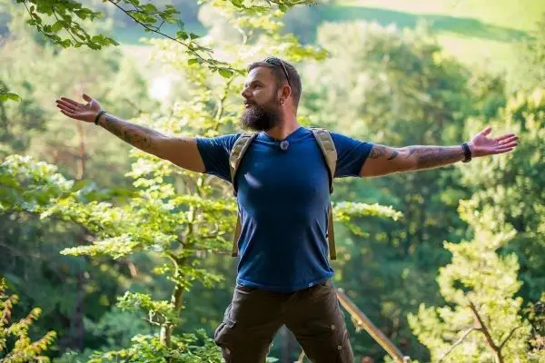 Mann mit Rucksack breitet die Arme in der Natur aus