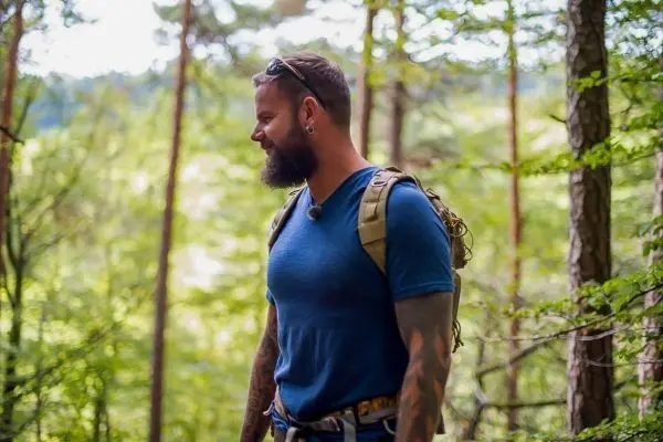 Mann mit Rucksack steht im Wald und schaut nachdenklich zur Seite