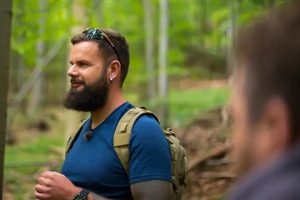 Mann mit Rucksack steht im Wald und spricht mit einer anderen Person