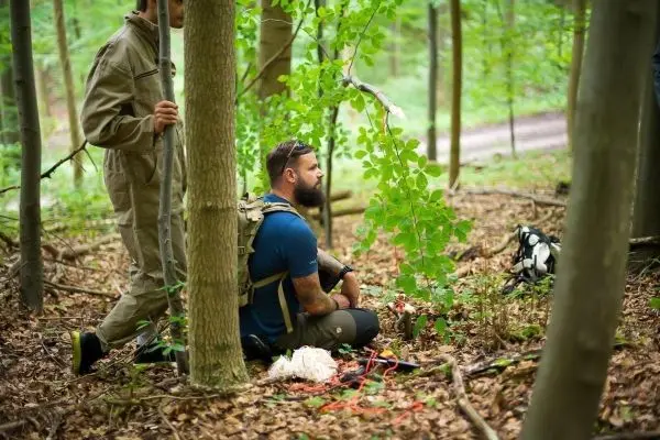 Mann sitzt im Wald auf dem Boden, umgeben von Bäumen und Pflanzen