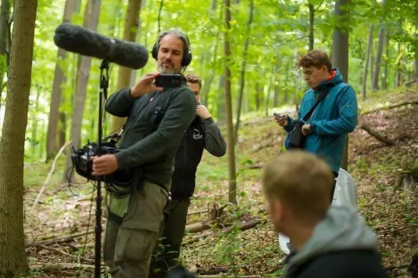 Mikrofon wird von einem Mann im Wald gehalten, während andere sich vorbereiten