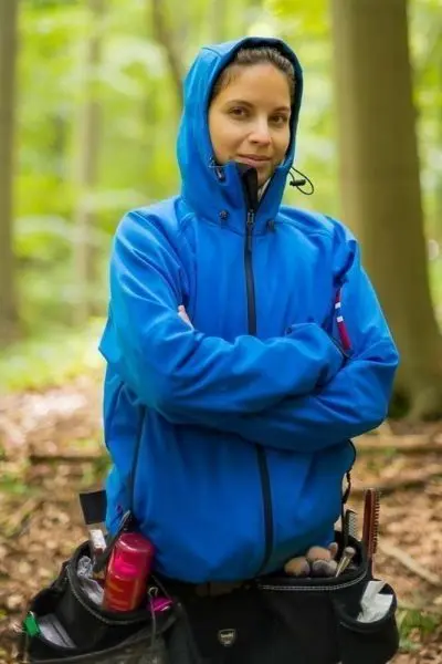 Person mit blauer Jacke und Werkzeugtasche im Wald