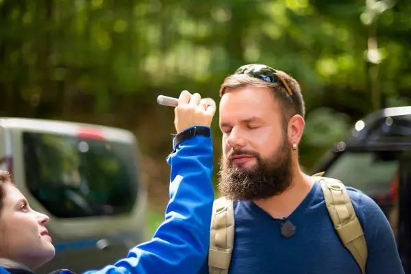 Person trägt Rucksack, während eine andere Person mit einem Stift auf ihr Gesicht zeichnet
