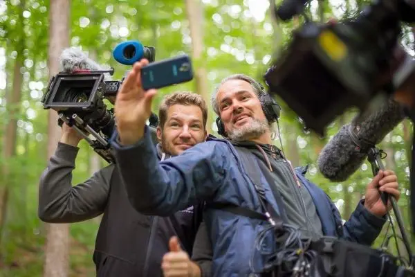 Zwei Personen halten Kameras und ein Smartphone in einem Wald