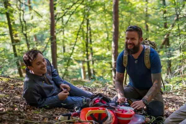 Zwei Personen sitzen im Wald auf dem Boden und betrachten Ausrüstung