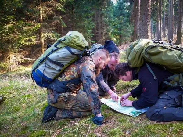 Drei Personen betrachten eine Karte im Wald beim Überlebenstraining