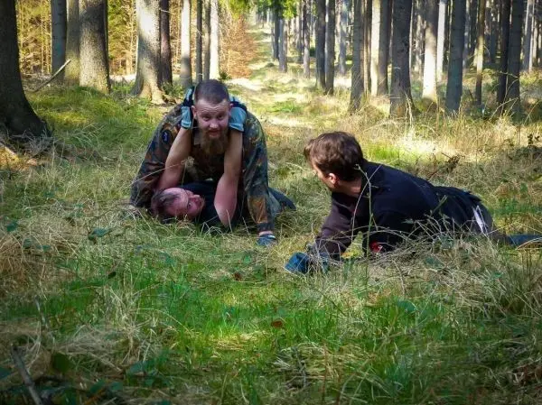 Drei Personen im Wald, eine Person trägt eine andere auf dem Rücken