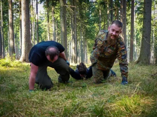 Drei Personen kriechen auf dem Boden durch einen Wald mit hohem Gras