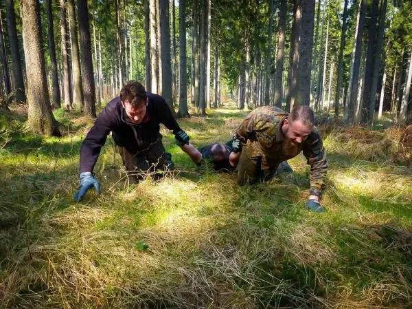 Drei Personen kriechen durch hohes Gras im Wald