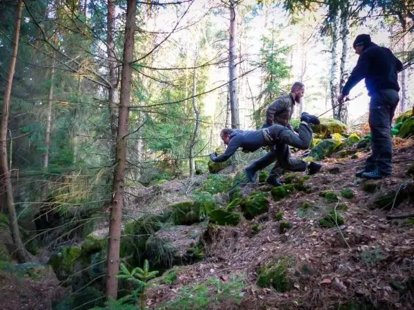 Drei Personen ziehen einen anderen über einen steinigen Hang im Wald