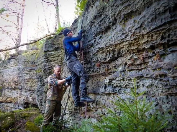 Kletterer nutzt Seil zur Besteigung einer Felswand, während ein Helfer unterstützt
