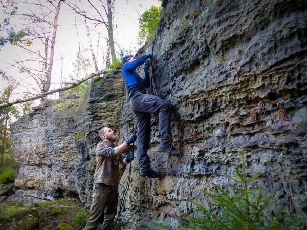 Kletterer sichert Partner mit Seil an einer Felswand im Wald