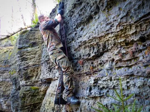 Klettert an einer Felswand mit Seilunterstützung und Handschuhen