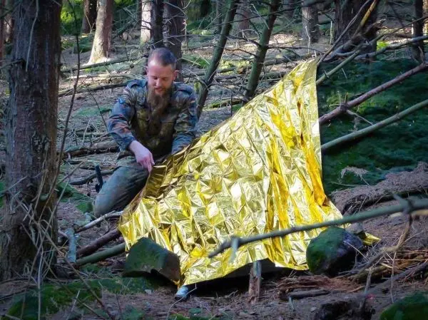 Mann baut Tarp-Notunterkunft aus reflektierender Folie im Wald