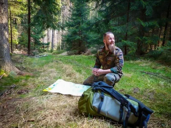 Mann sitzt auf dem Boden, betrachtet eine Karte neben einem Rucksack im Wald