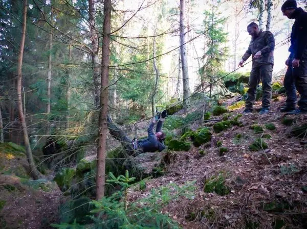 Mann überquert mit Seil eine Schlucht, während zwei Personen unterstützen