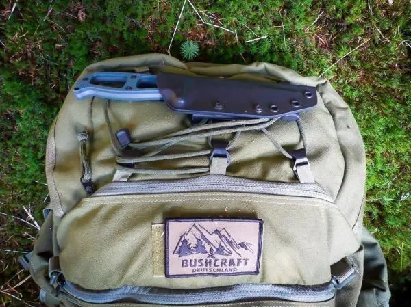 Messer liegt auf einem grünen Rucksack mit Bushcraft-Aufnäher