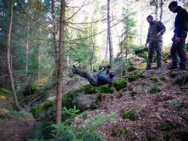 Person schwingt an einem Seil über den Boden im Wald